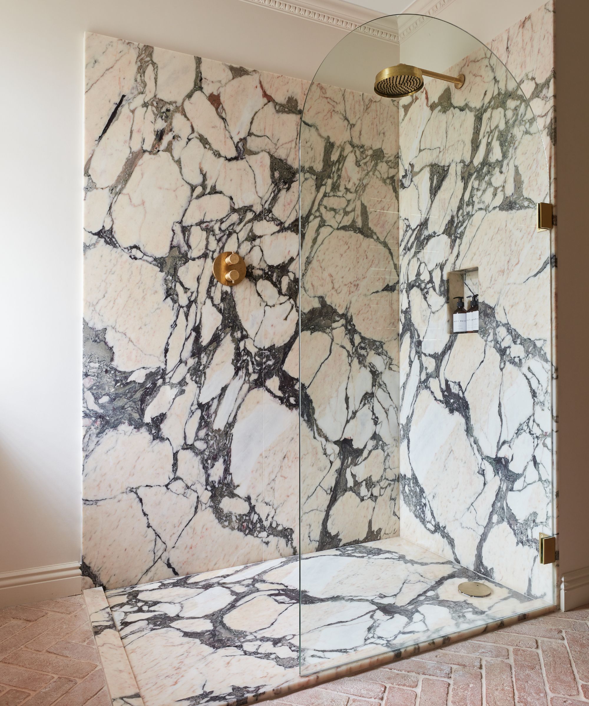 A warm white bathroom with terracotta floor tiles and a marble shower