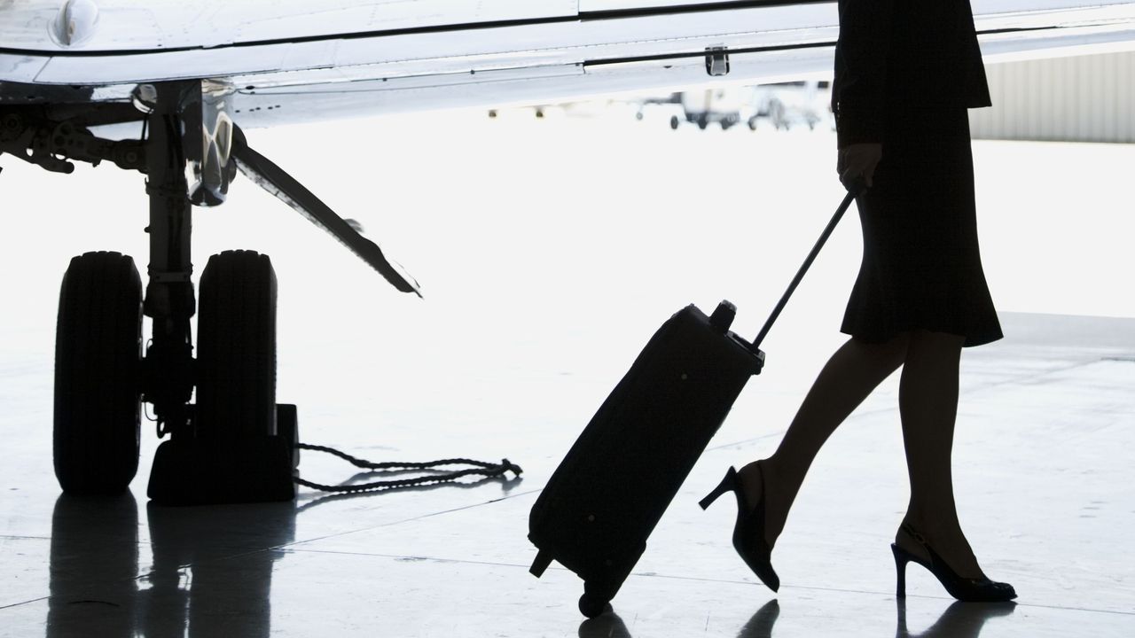 Flight attendant in high heels with wheelie bag next to plane