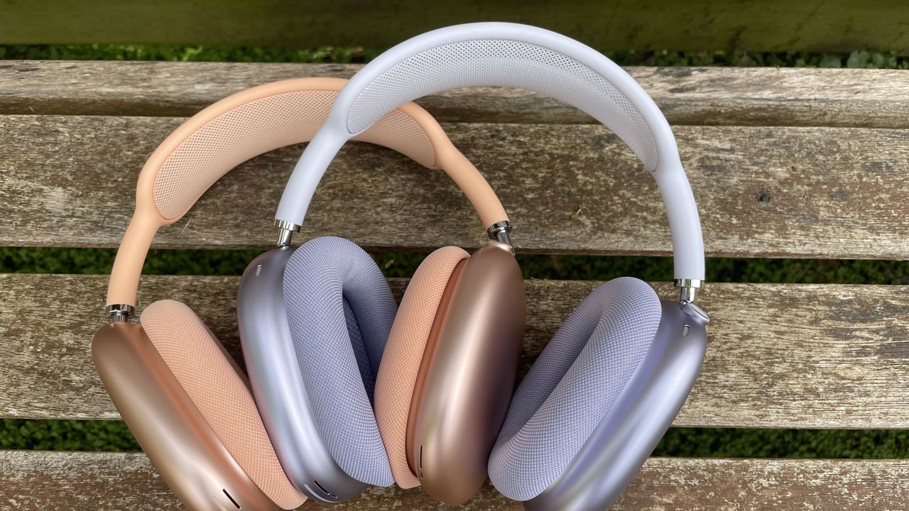Apple AirPods Max 2 in orange with AirPods Max just visible in purple, outside in a garden on a bench, held in a hand