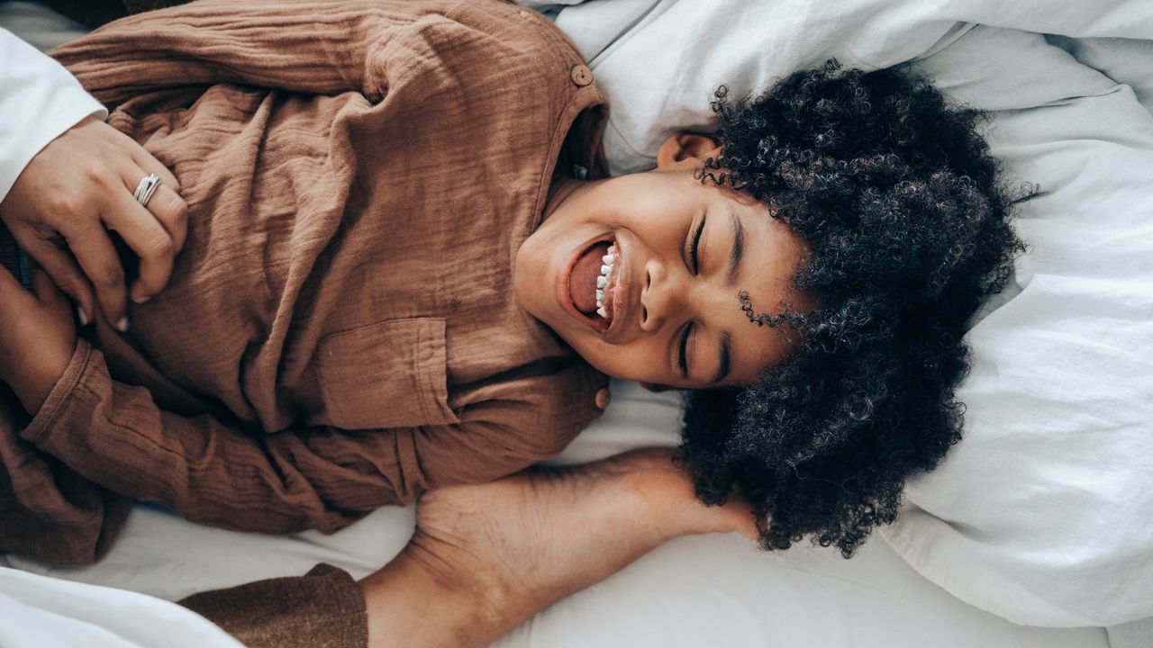 Best mattress for kids: Happy boy lying on bed with adults foot playfully tapping his head