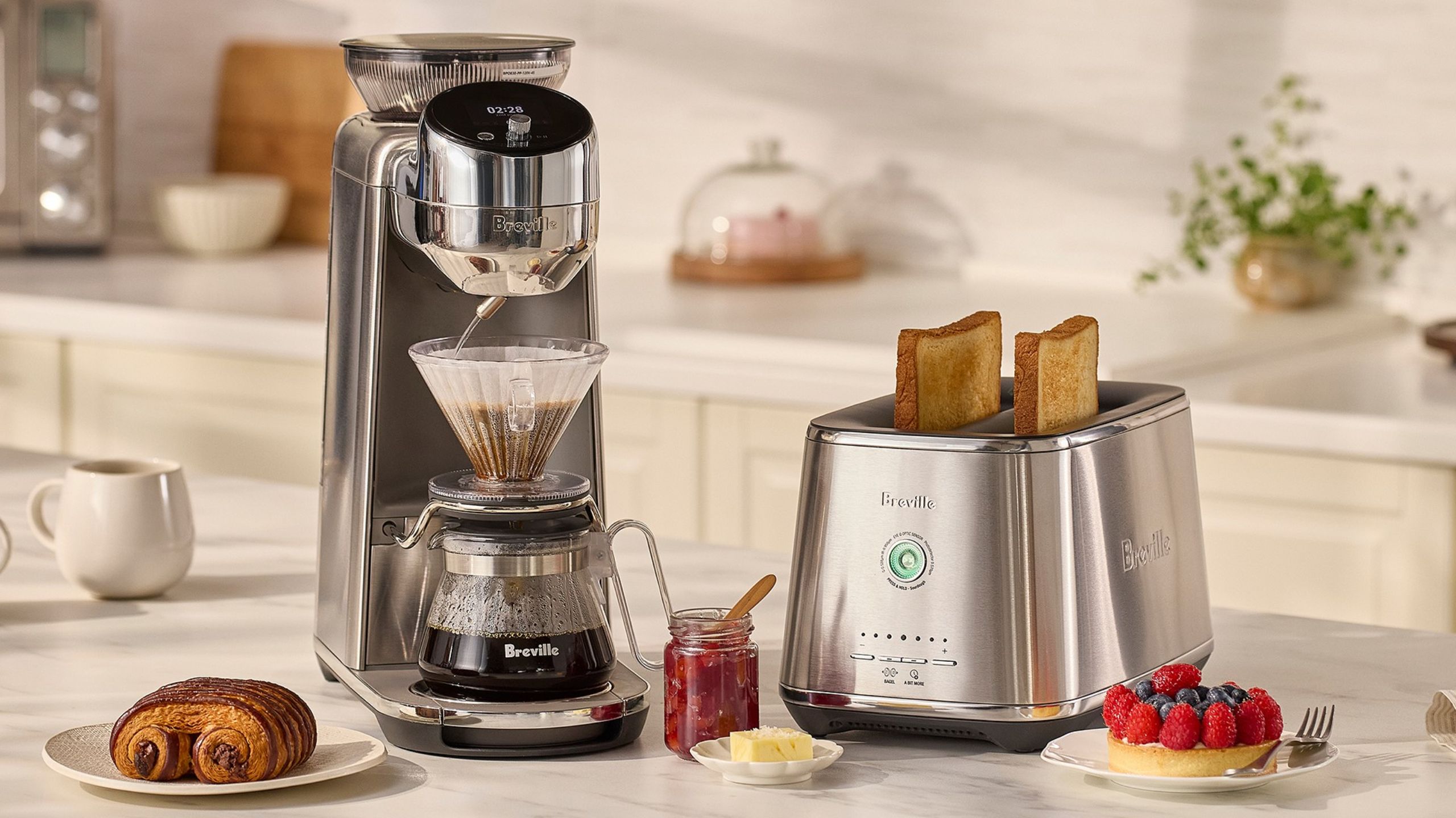 A silver Breville Spiral Luxe&trade; Auto Pour-Over Coffee Maker beside a matching toaster, on a white kitchen counter