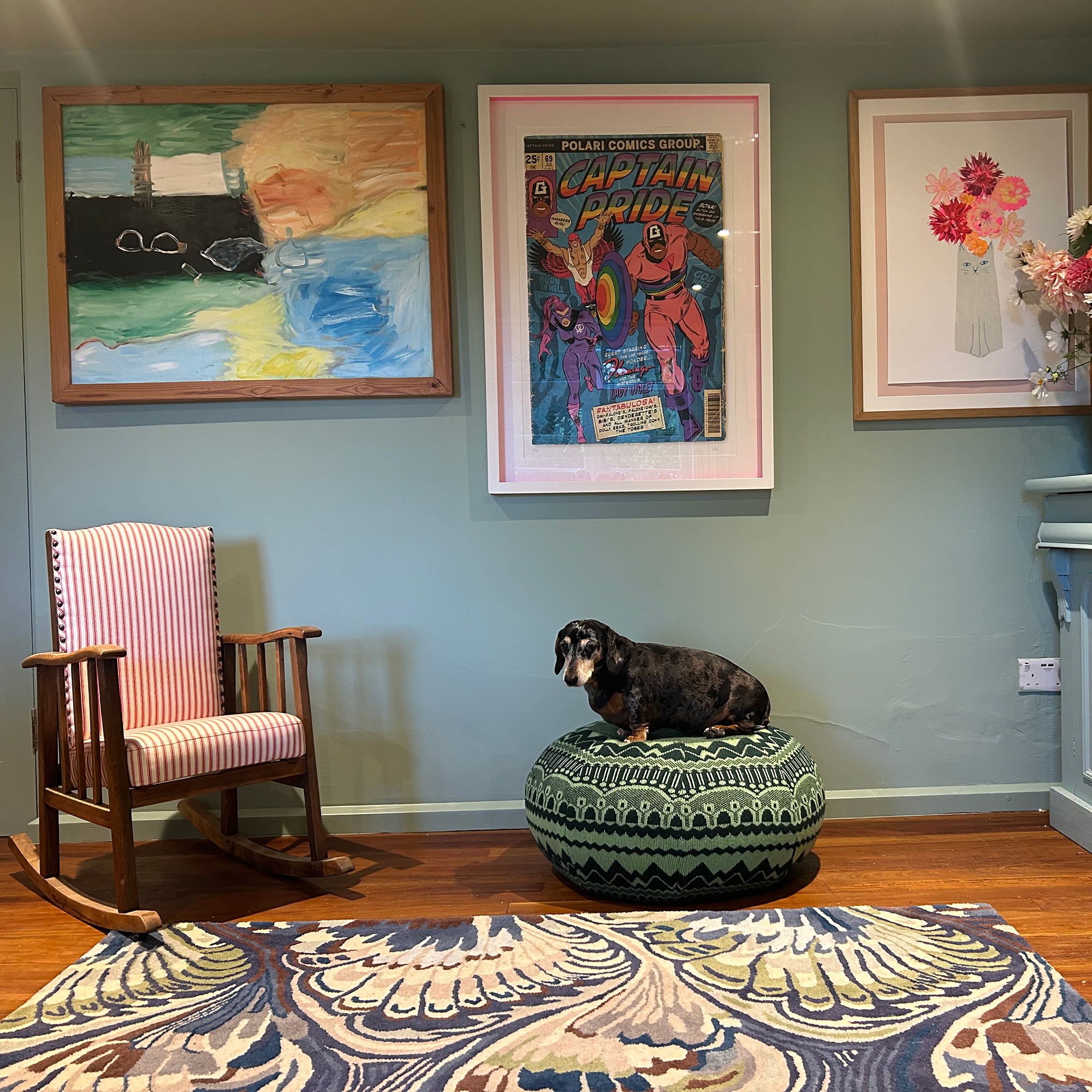 Dog sitting on patterned green pouffe by rocking chair and green wall with framed artworks