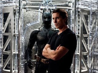 Bruce Wayne (played by Christian Bale) stands besides his alter ego's bat outfit in a still from the movie The Dark Knight Rises,