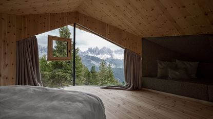 View from inside wood-lined Odles Lodge, looking out to pine trees and mountains