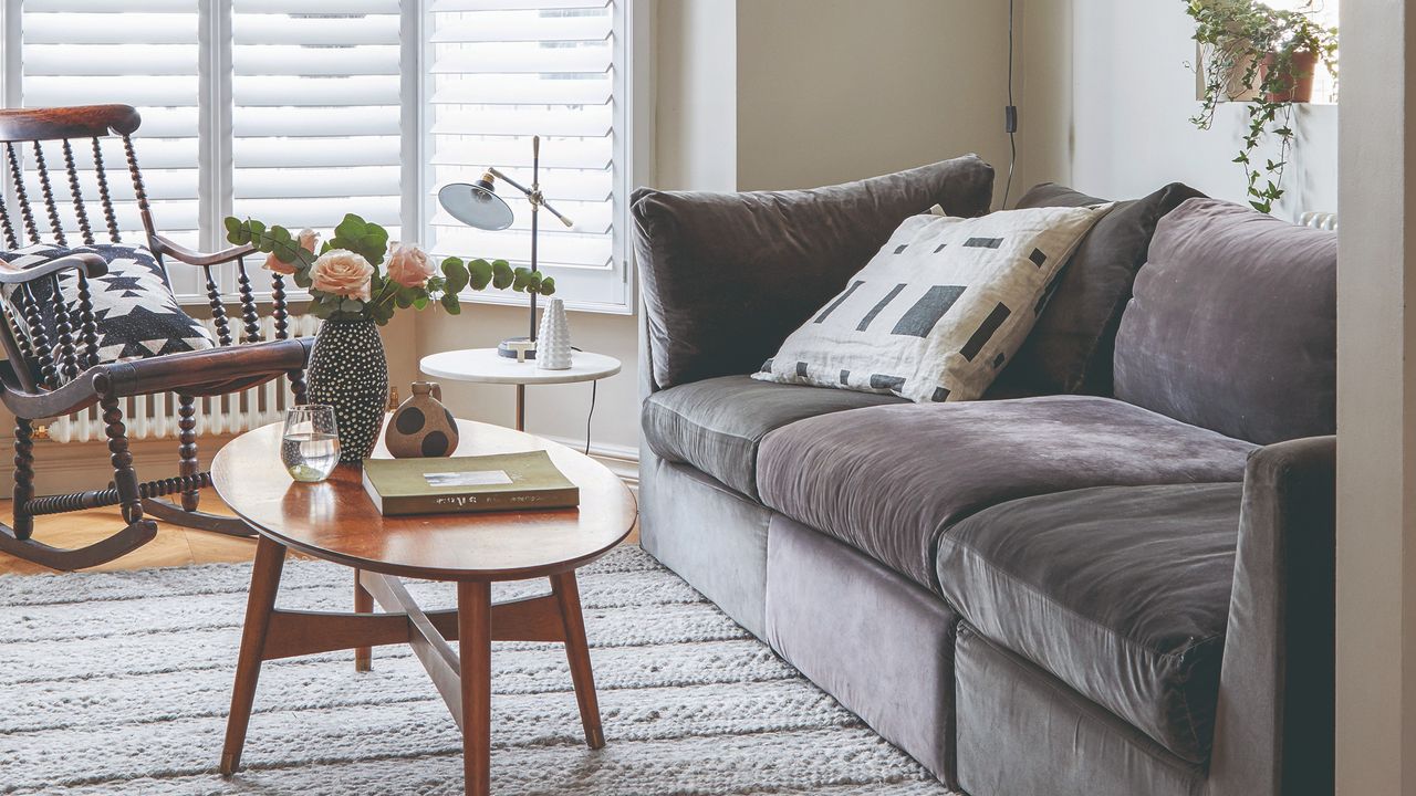 A small living room with a grey velvet sofa, an oval coffee table and a rocking chair