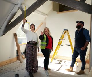 2 women and 1 man stood in loft measuring height of beams