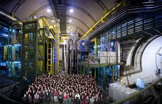 The LHCb team stands in front of their experiment, the LHCb detecor, at the Large Hadron Collider in Geneva.