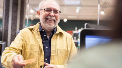 Smiling senior man giving credit card to cashier at supermarket checkout counter