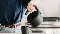 Best stovetop kettles. Fellow Clyde Stovetop kettle, person pouring hot water from kettle into black mug, stove in background