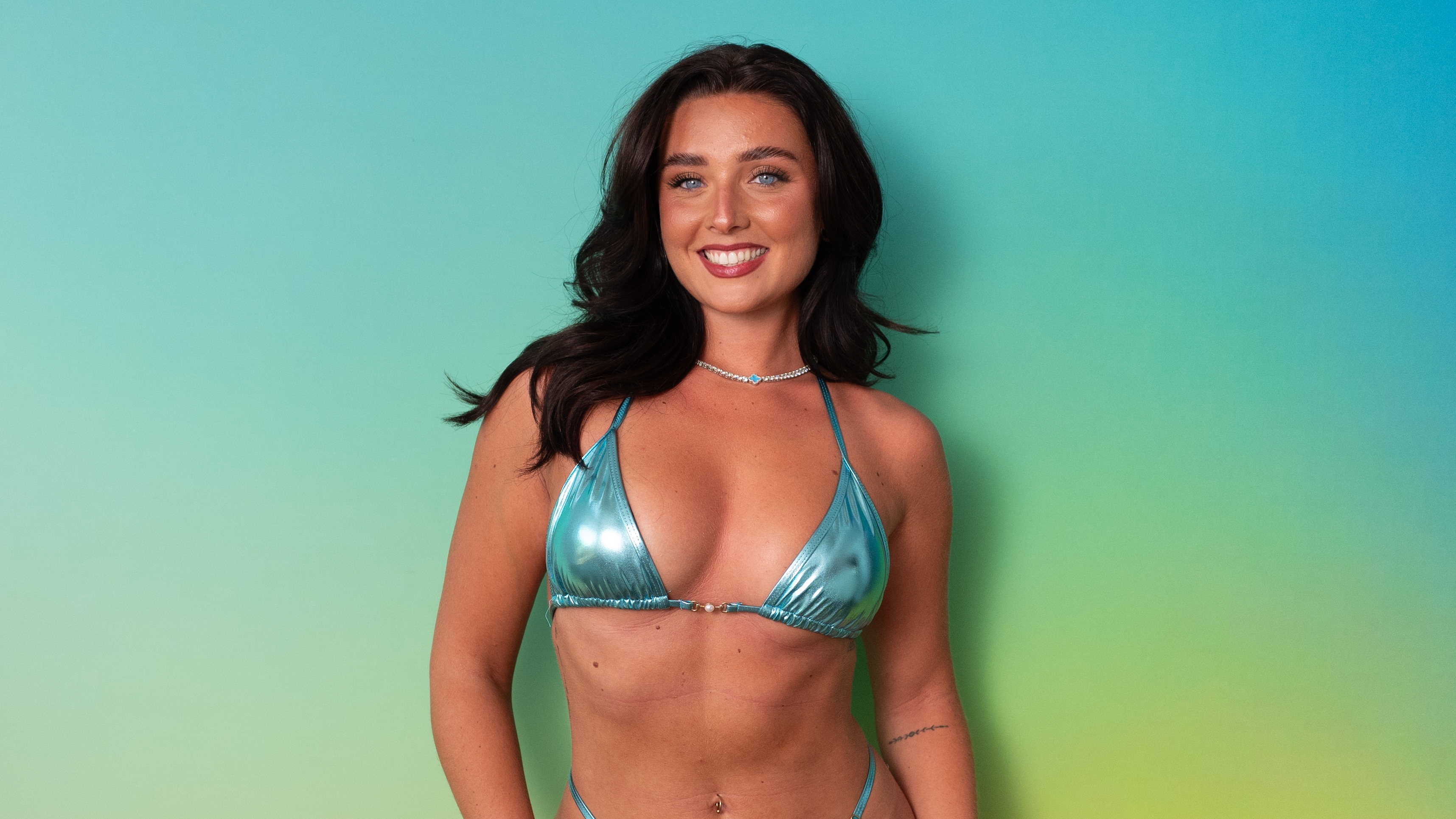 Rheo standing in swimwear in front of a green background.