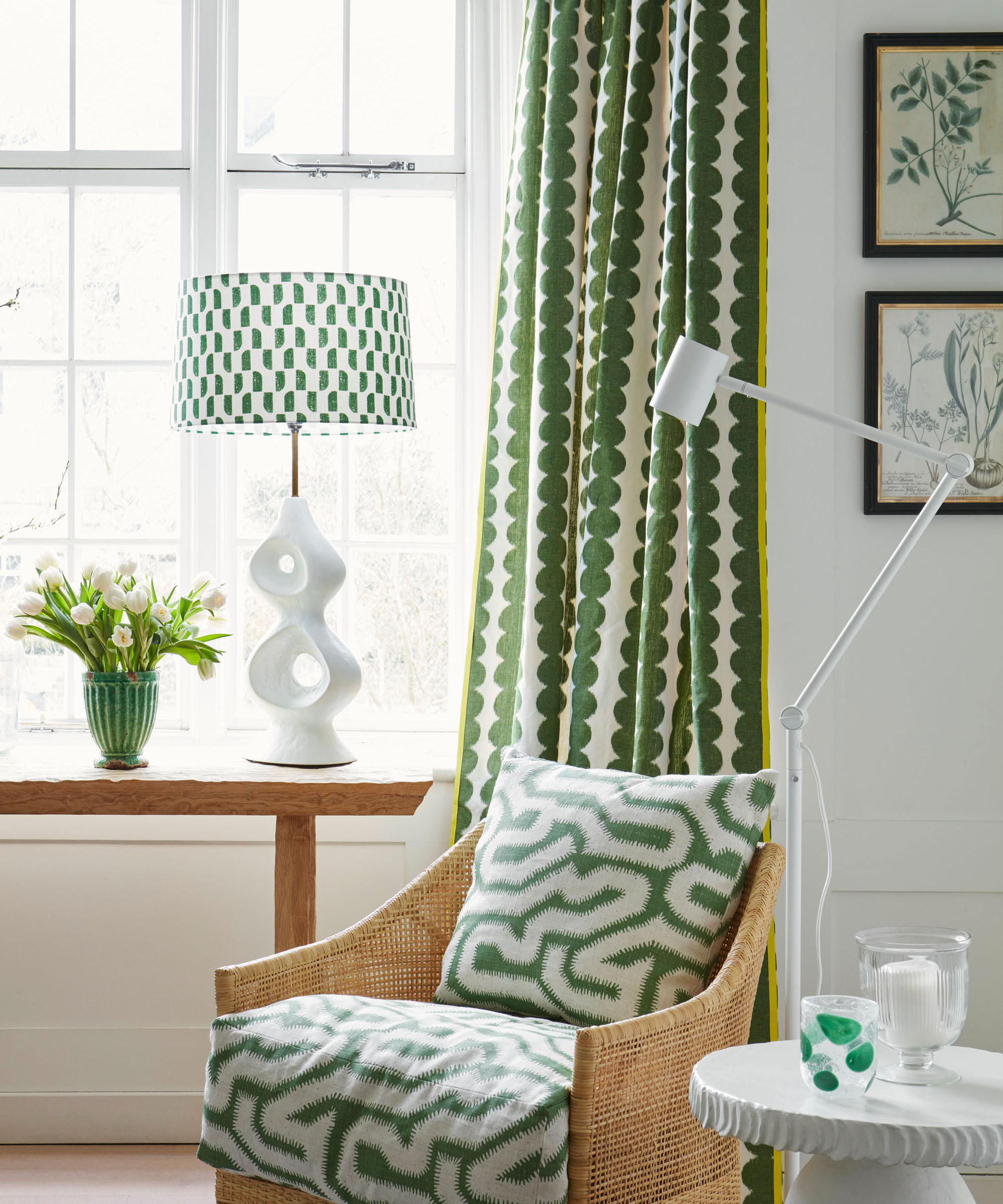 wooden console in living room window bay with green and white fabric designs and botanical artworks