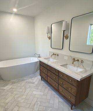 A modern bathroom with herringbone flooring decor, dresser vanity unit and white bathtub