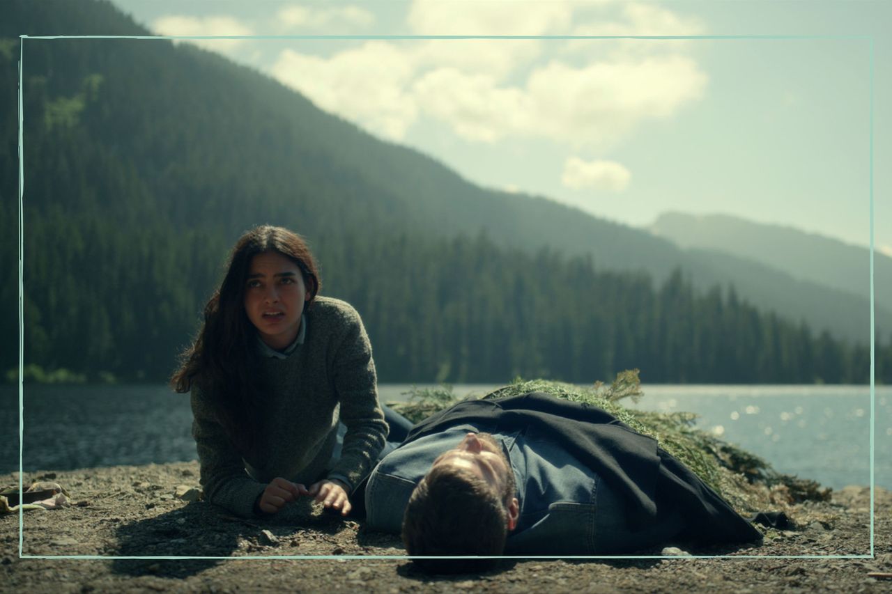 The main character of Keep Breathing kneeling next to the body of a man, with a lake and forest in the background