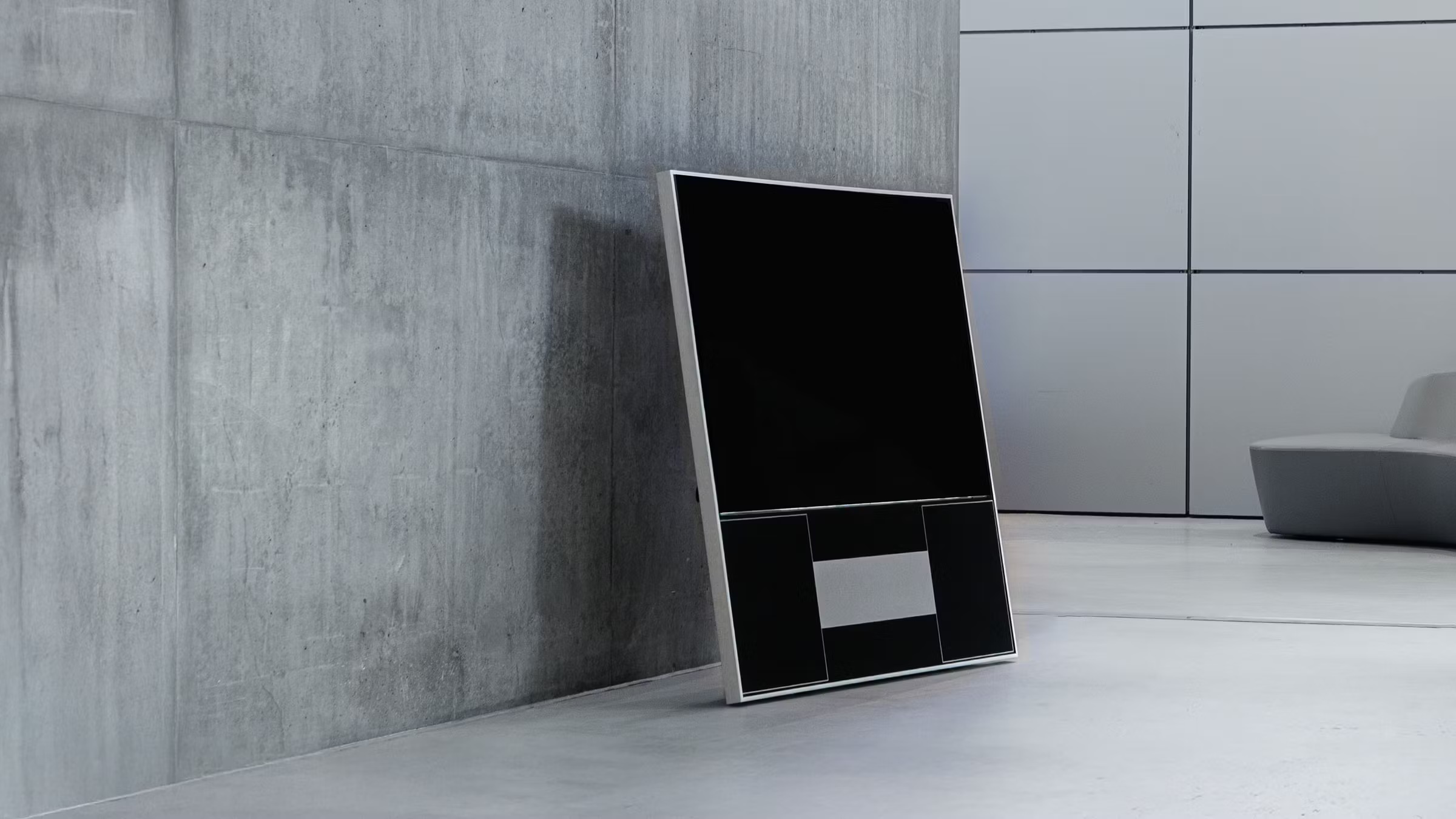The Samsung The HiFi Frame TV with a geometric black and grey artwork against a grey concrete wall