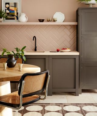 blush and gray kitchen with open shelving, gray cabinetry, graphic rug, cream countertop, black faucet, cream floor tiles, small table and chairs,