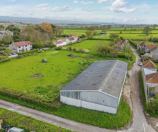 Two large green building plots next to a road with an agricultural building