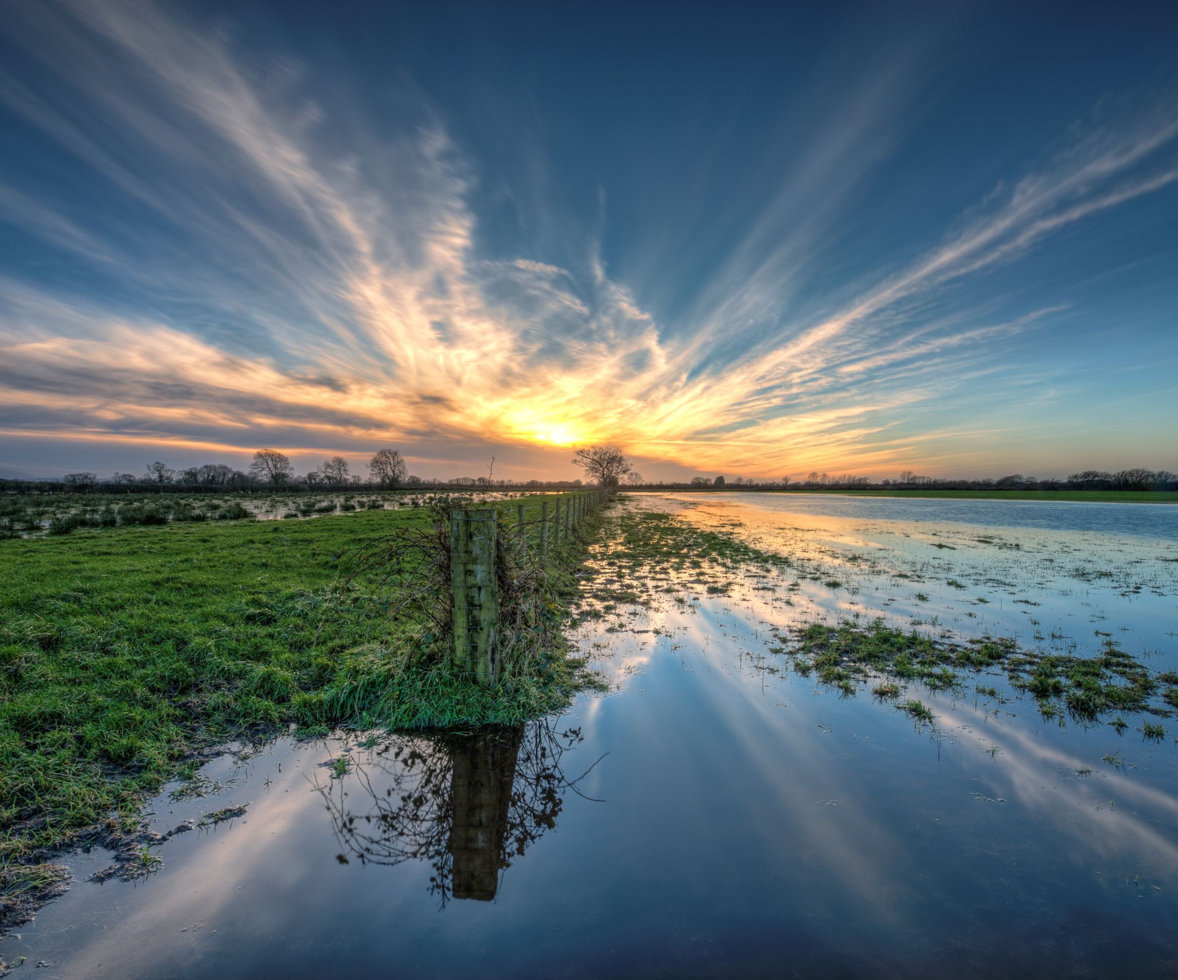 A flooded piece of land with the sun shining from behind a clous in the distance