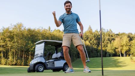 A golfer celebrating a made putt with a cart in the background