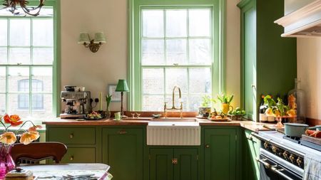 A small kitchen with green cabinets, copper countertops, a range cooker, and a vintage table and chairs set