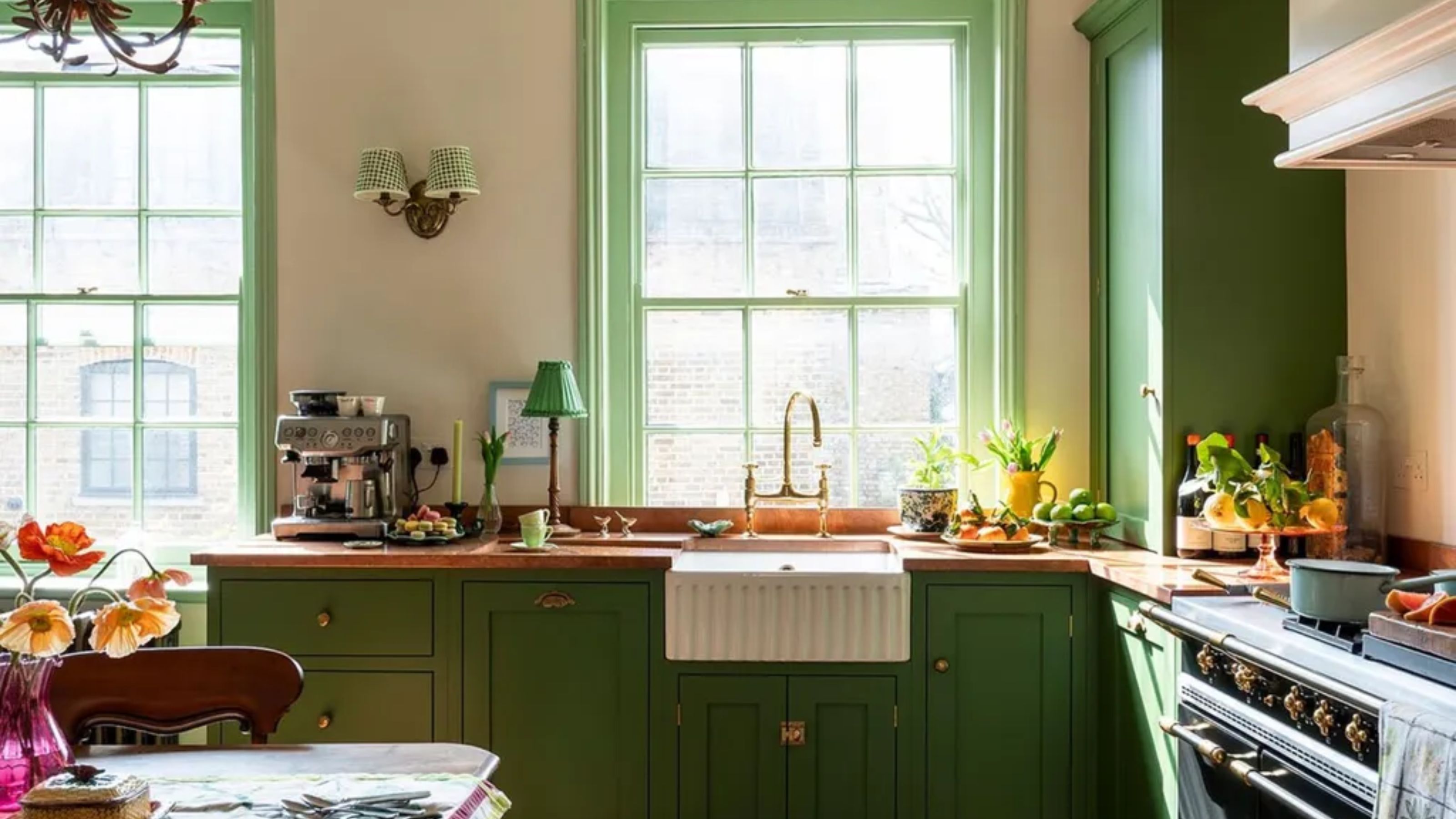A small kitchen with green cabinets, copper countertops, a range cooker, and a vintage table and chairs set