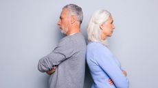 Senior couple standing back to back with arms folded, isolated on grey background