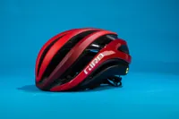 A red Giro Aether MIPS helmet is featured here on a blue background