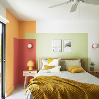 bedroom wall decor ideas, bedroom with orange, red and green colour blocking, wooden bed and matching side table, mustard throw, artwork