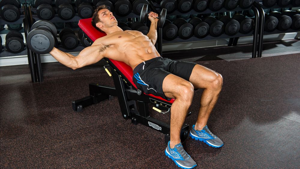 Man lying on a weights bench set to an incline performs a chest flye using dumbbells