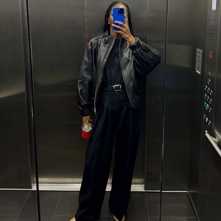 Woman wears a black leather jacket, black trousers, shirt, belt and yellow sneakers. 