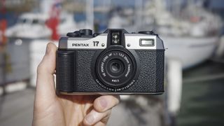 Pentax 17 compact film camera front-on, in the hand with boats in background