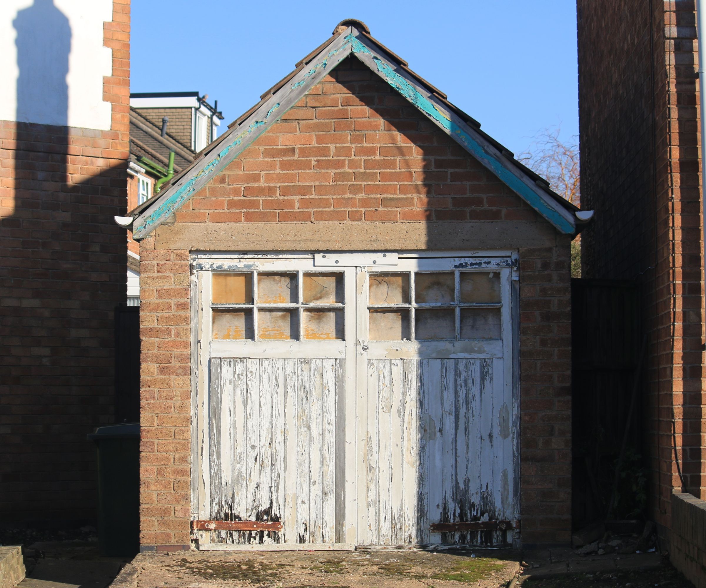 A red brick garage with white wooden doors with glazing and a pitched roof