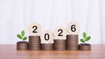 Six stacks of coins topped with greenery and round wooden blocks with the year 2026. 