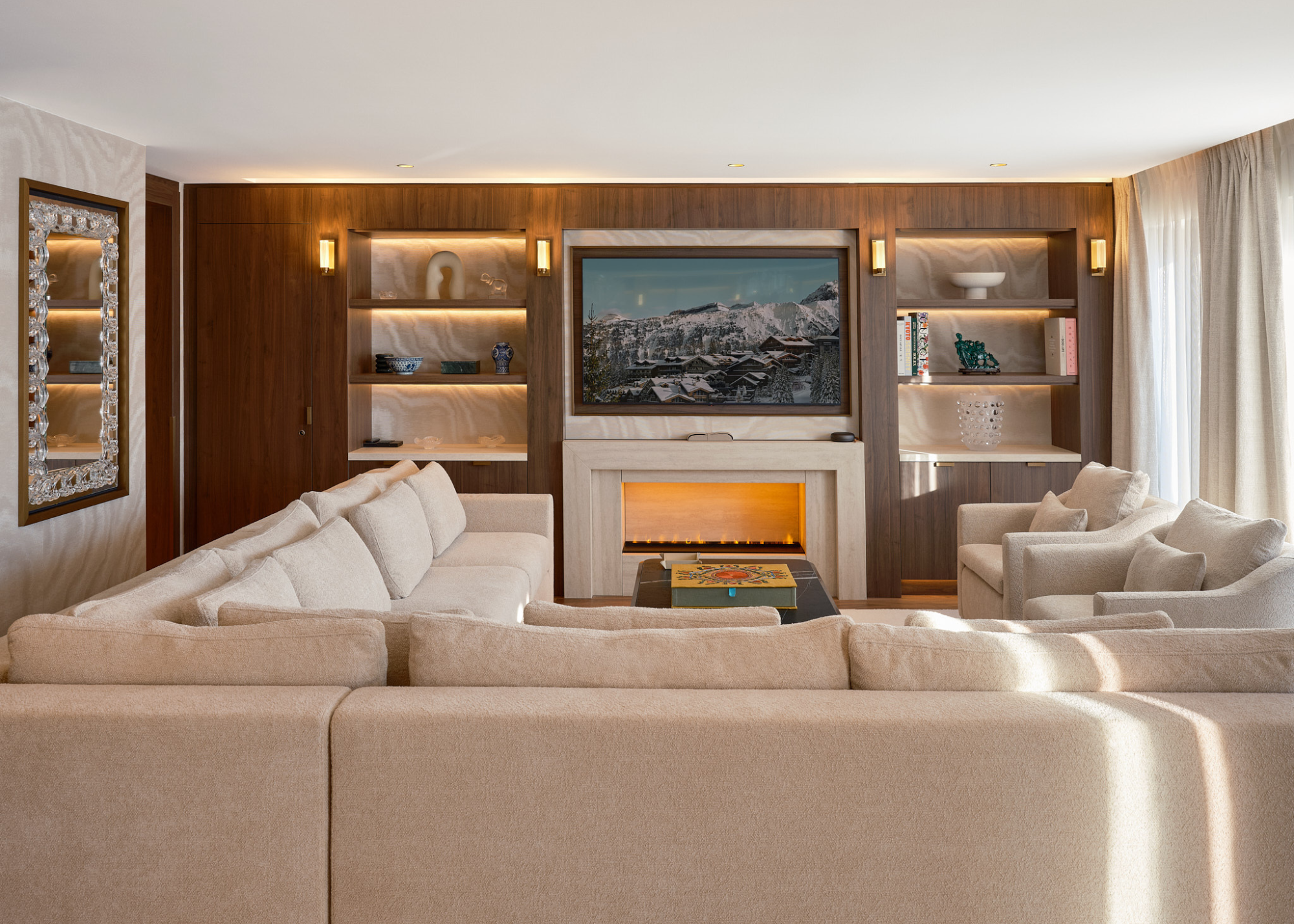 Maya Hotel Courchevel 1850 Lalique suit with an l-shaped cream sofa with matching armchairs centered around a coffee table with a media wall at the far back wall