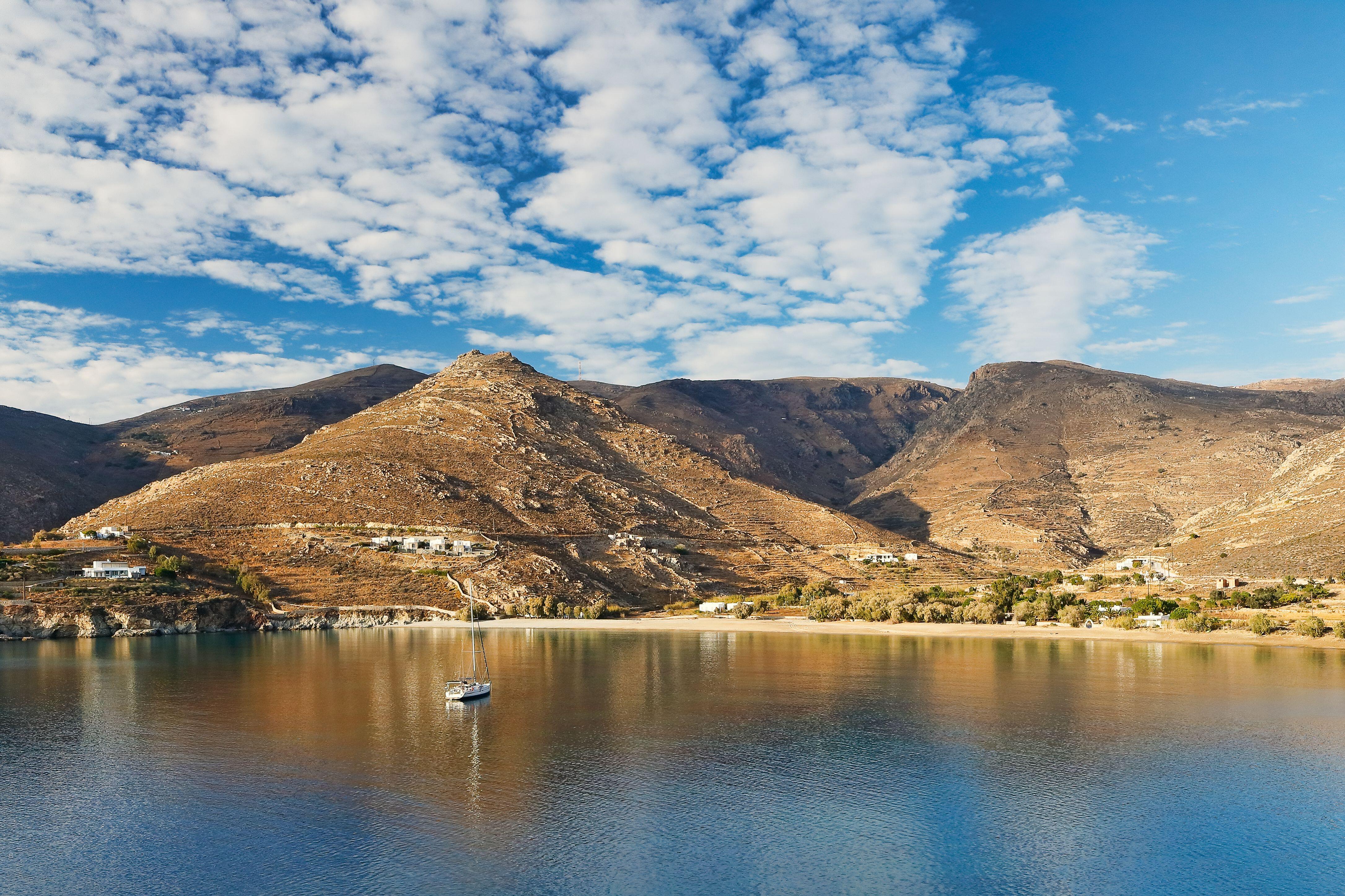 A lone sail boat moored infront of a sandy beach, backed by steep barren hillls