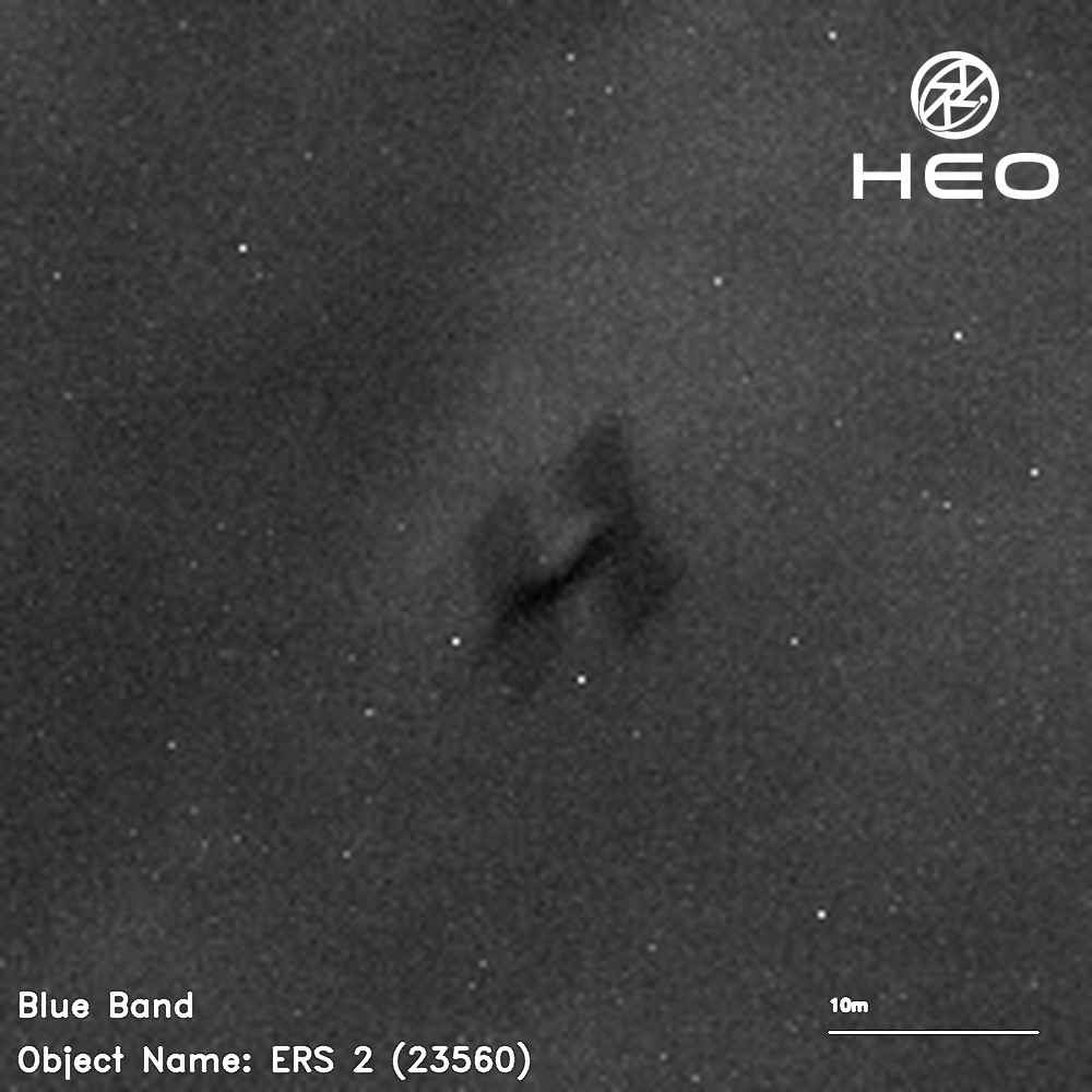 Blurry black and white image of an H-shaped satellite against a background of a few dozen stars