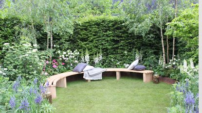A small curved bench at the RHS Chelsea Flower Show, bookended with two trees