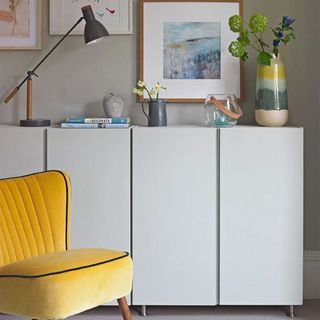 grey cabinets with yellow chair, gallery wall, table lamp and vase