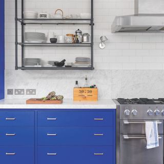 Kitchen with white metro tiles above a marble splashback, blue kitchen cabinets, and a silver range hob