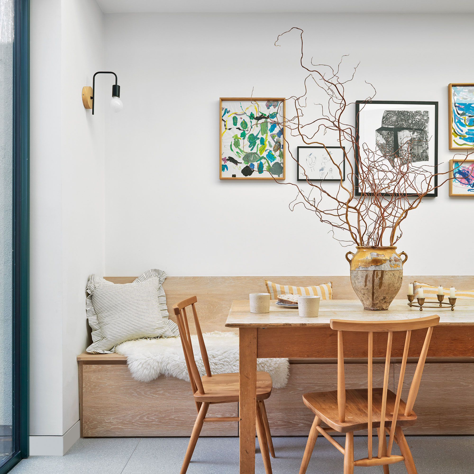 White dining area with wooden table, wooden bench and vase