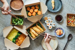 takeaway with sushi, tempura prawns and hands holding chopsticks