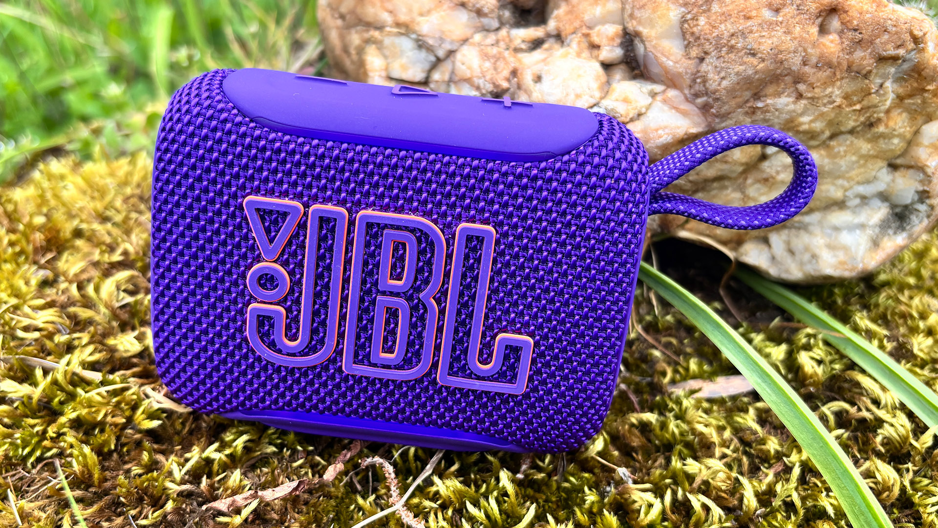 JBL Go 5 speaker in purple finish on mossy stone