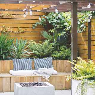 Outdoor sitting area underneath a pergola with plants and ivy growing above it