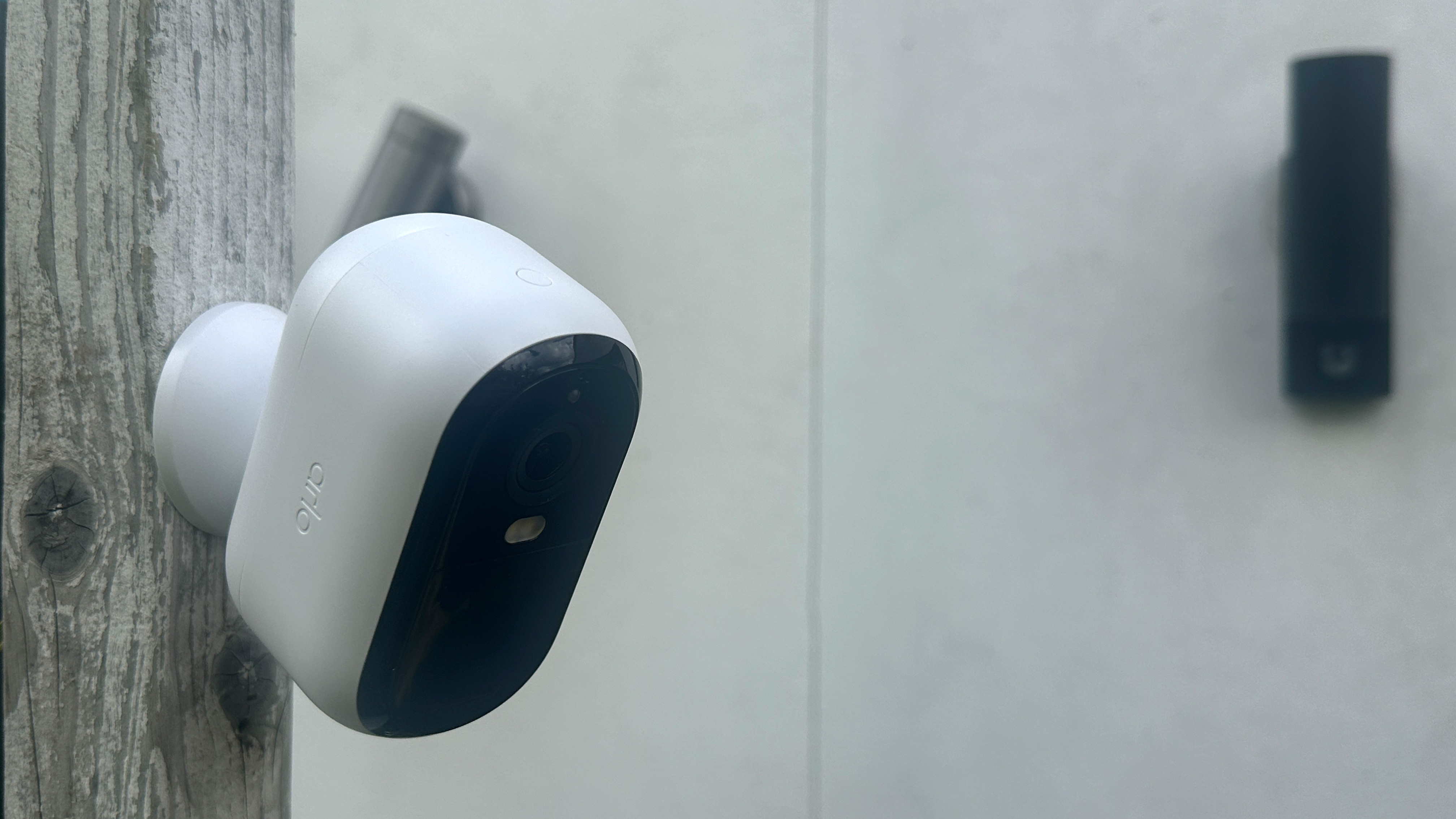 side view of Arlo Essential 2nd Gen camera mounted on a fence – another camera is visible on a wall behind