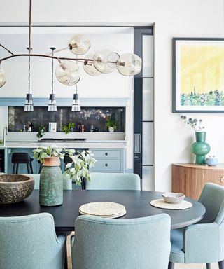 dining area with oval wooden table, aqua dining chairs, pale blue kitchen cabinets and glass globe