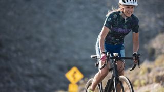 Woman wearing bike helmet cycling up a hill in cycling kit