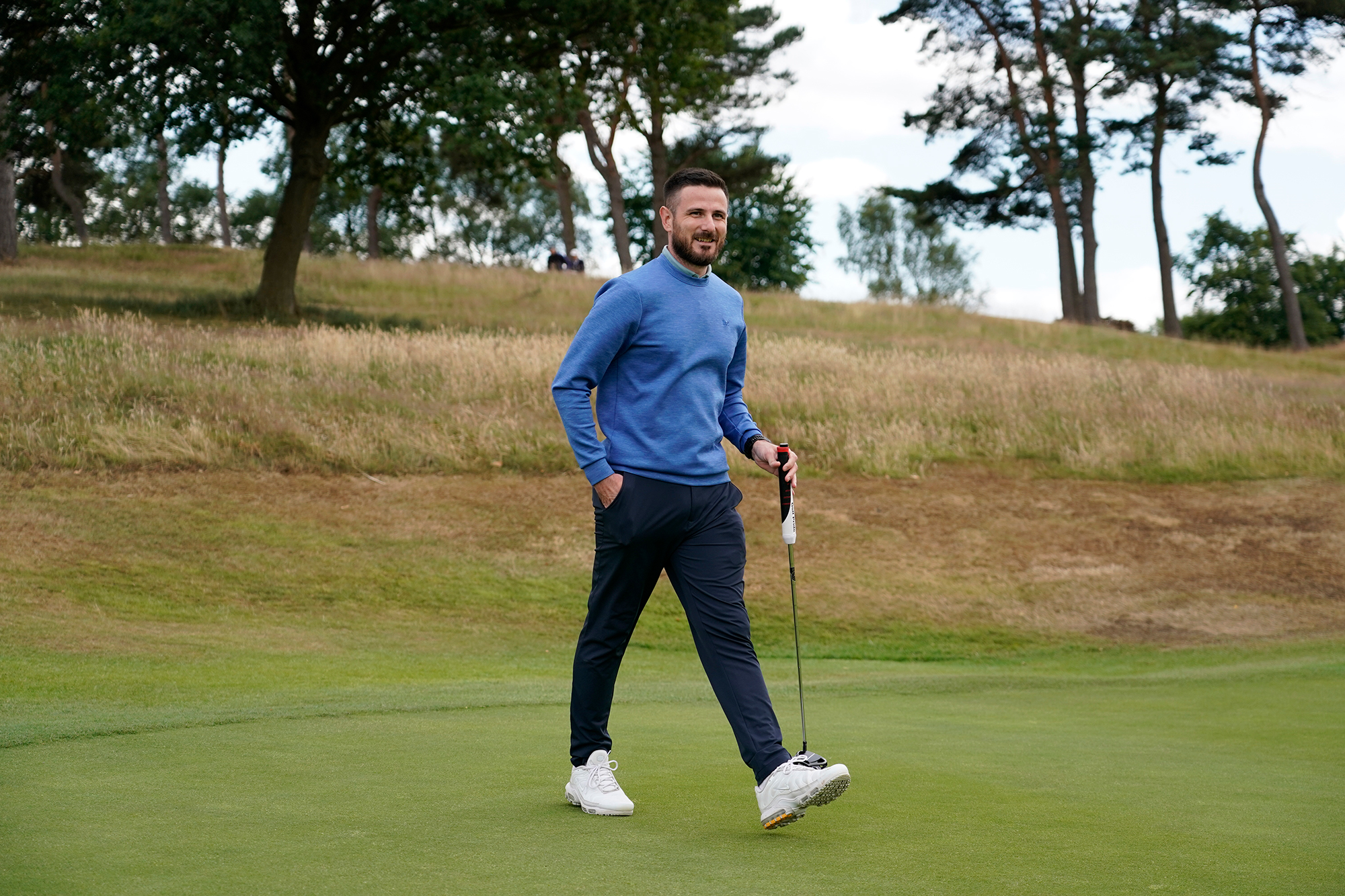 Baz Plummer smiling on the green with his putter in his hand as he walks towards his golf ball