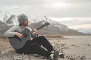 A guitarist plays a Klos cutaway model against a dramatic mountain backdrop