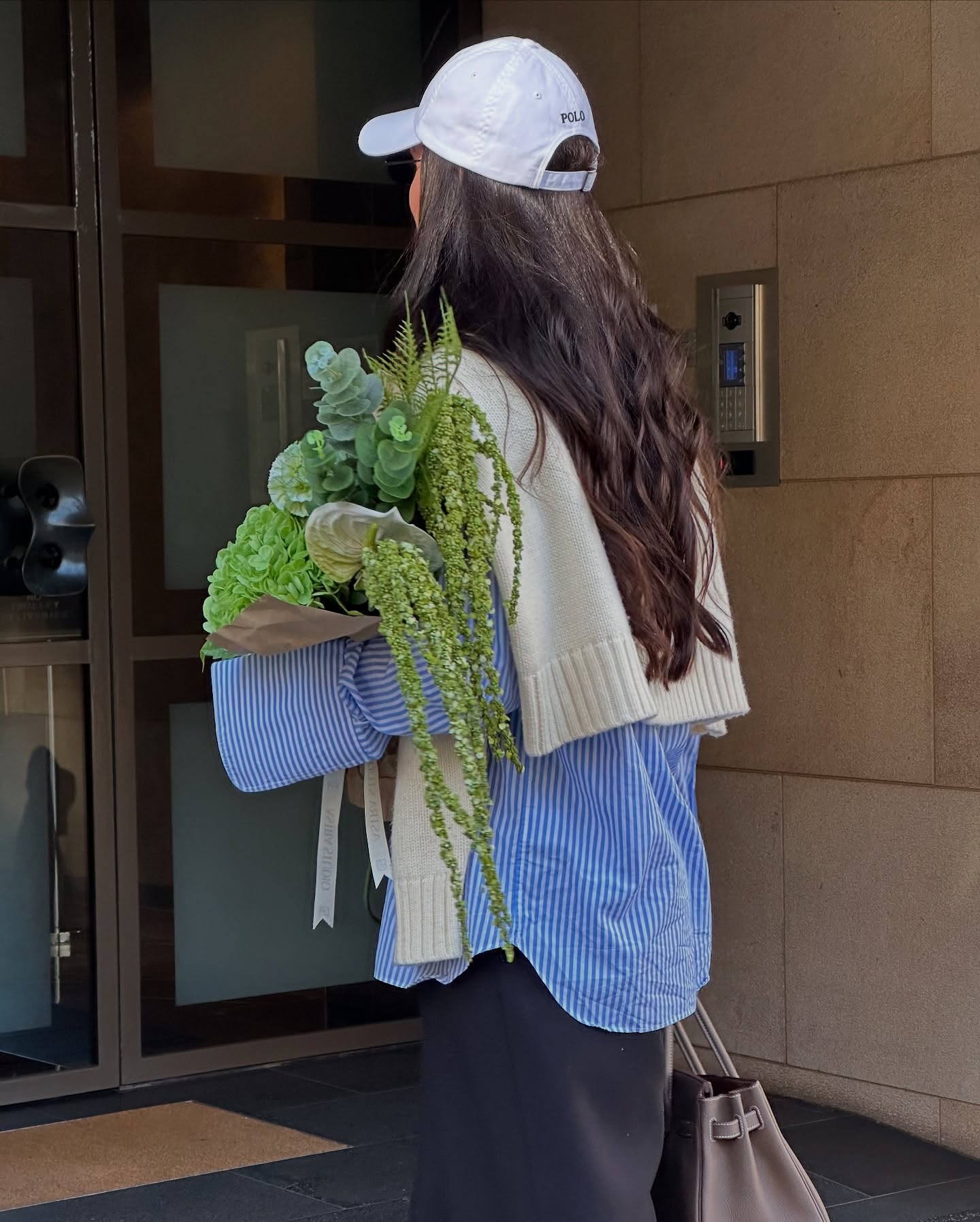 aymie cahill wears a striped oxford shirt, black shirt and baseball cap.