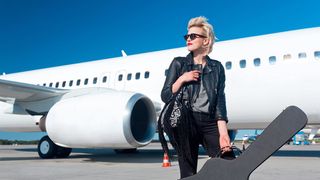 Woman holding hard guitar case stands in front of a white plane