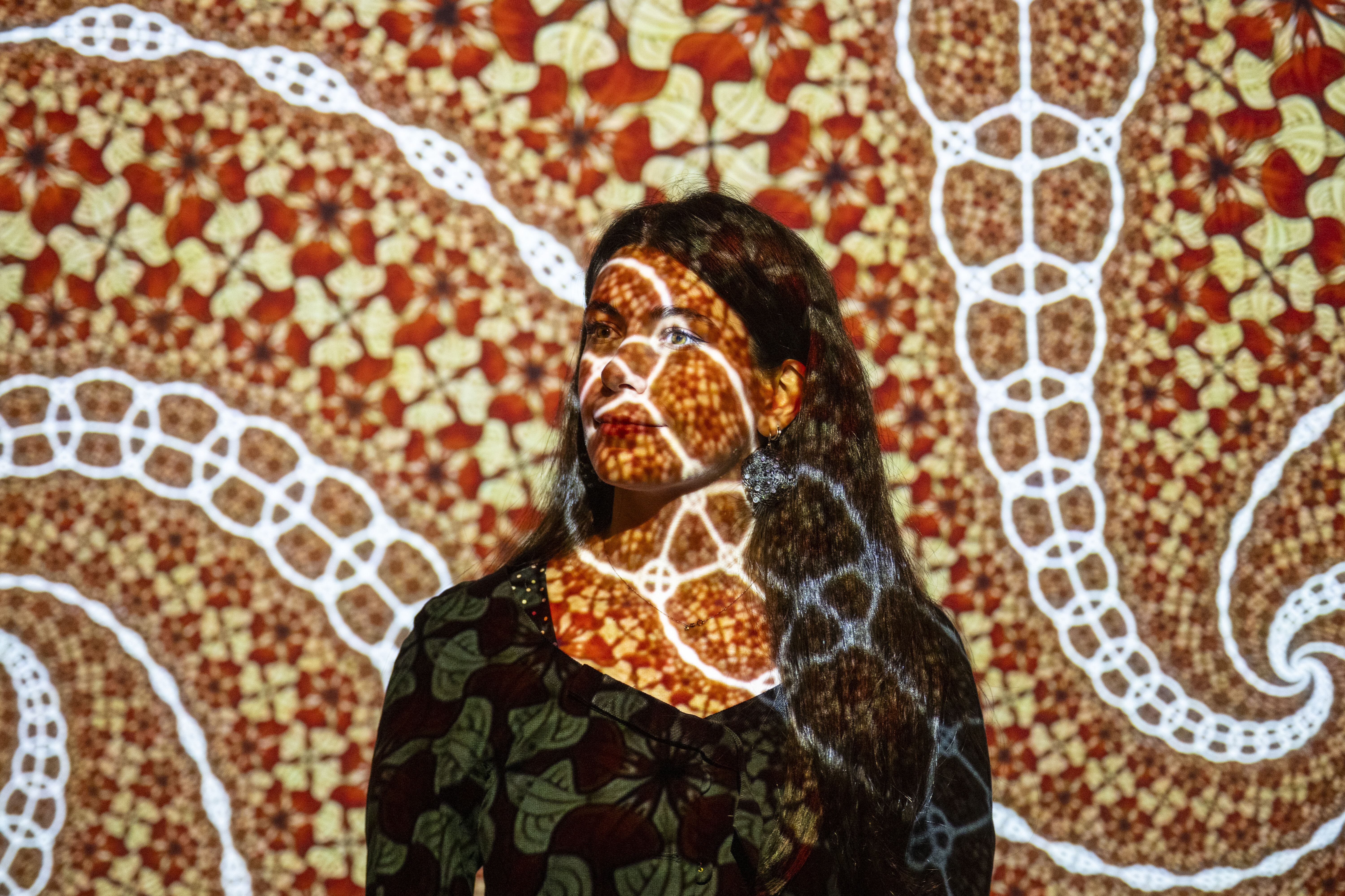 A visitor stands immersed in a richly coloured immersive projection of Escher's tessellation patterns